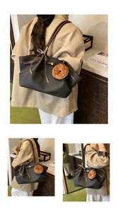 Detail view of a large black tote bag with brown handles and a plush donut charm