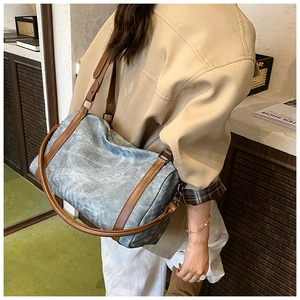 Side view of a vintage blue denim cylinder bag with brown leather strap on model