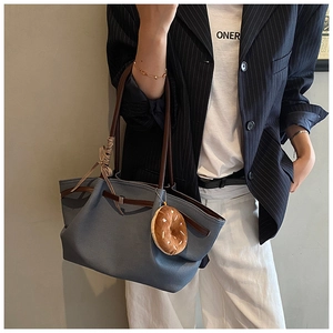 Detail of blue tote bag with brown straps, ribbon bow and plush donut charm accessory