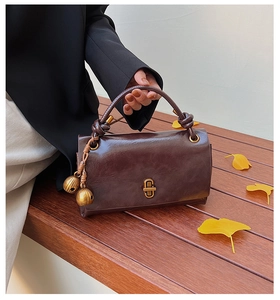 Detail of dark brown vintage faux leather handbag with gold metal twist lock on wooden bench