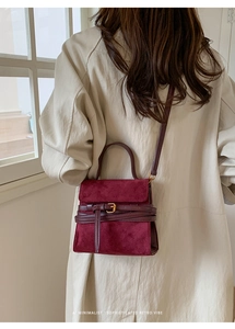 Bolso de mano minimalista en ante burdeos con hebilla llevado sobre una gabardina clásica