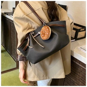 Detail of large black tote bag with brown straps and cute doughnut plush charm