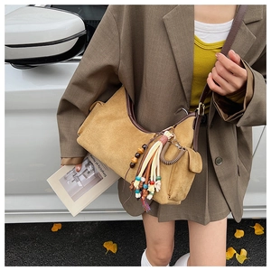 Détail du sac hobo en daim jaune moutarde avec glands colorés sur une rue urbaine d'automne