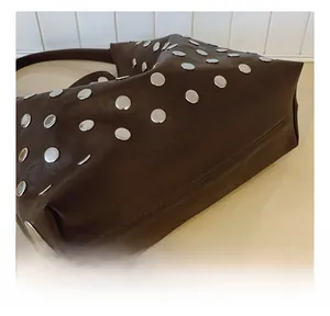 Detail showing precise stitching and silver rivets on a dark brown leather tote bag