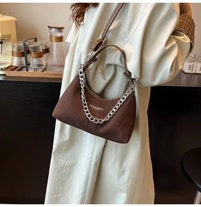 Détail d'un sac en daim marron avec chaîne argentée et bandoulière en cuir