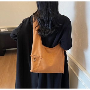 Détail du sac hobo en daim caramel avec anneau métallique porté à l'épaule au quotidien