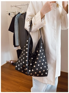 Vue latérale d'un sac cabas noir en similicuir avec rivets porté par une personne
