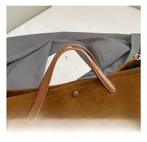 Detail view of brown suede tote bag featuring leather handles and a matching button closure