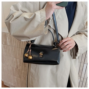 Close-up of black leather crossbody bag with golden clasp and bell charm detail