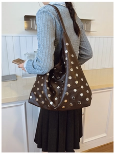 Detail of a large brown hobo bag featuring dense silver rivets on a soft matte texture