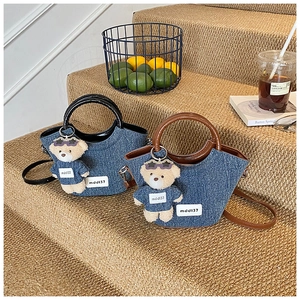 Détail de sacs seaux en denim avec poignées en résine et breloque ours sur un escalier