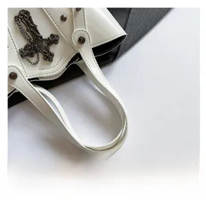 Detail of white leather bucket bag showing gothic cross charm and silver metal rivets