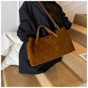 Close-up of brown suede tote bag featuring leather handles and decorative snap button