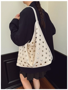 Detailed shot of cream leather hobo bag with silver rivet studs and a wide shoulder strap