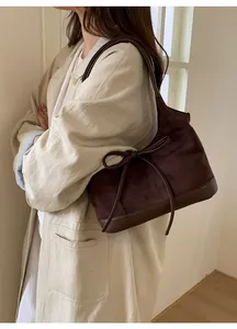 Detail of dark brown suede tote bag with decorative bow and leather trim on model