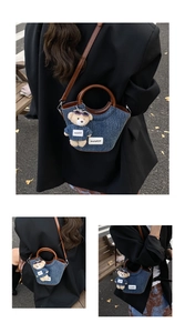 Detail of blue denim bucket bag with brown leather handles and cute teddy bear charm