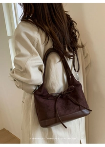 Close-up of brown suede tote bag with leather bow detail on model in beige coat