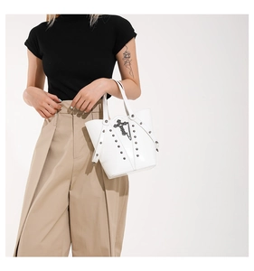 Detail of white leather bucket bag with metallic studs, silver chains and cross pendant