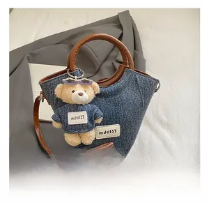 Detailed close-up of denim bucket bag with leather handles and cute bear charm accessory