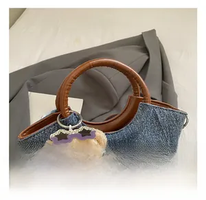 Detail of denim bucket bag with brown leather ring handles and cute plush bear charm
