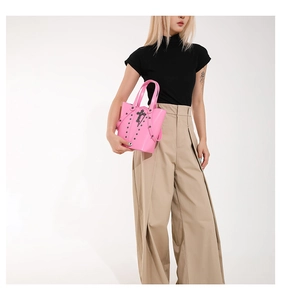 Detail of pink Y2K bucket bag with dark rivets and silver cross charm worn by model