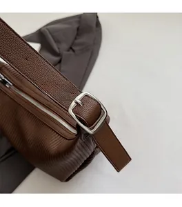 Detail of dark brown lychee leather texture and silver metal buckle on a shoulder bag