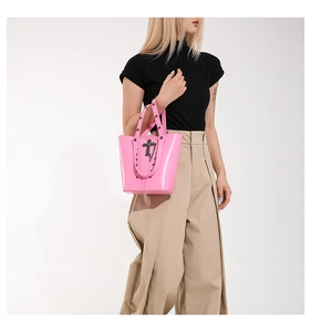 Detail of pink glossy leather bucket bag featuring black metal cross and gothic rivets