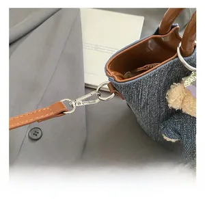 Detail of silver metal swivel hook and leather strap on denim bucket shoulder bag