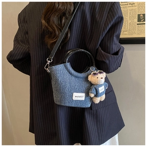 Détail du sac à bandoulière en denim bleu avec anse noire et pendentif ours en peluche