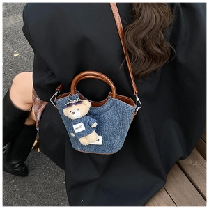 Dettaglio della borsa a secchiello in denim con tracolla in pelle marrone e orsetto