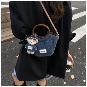 Détails du sac seau en denim bleu avec anses en cuir marron et breloque ourson