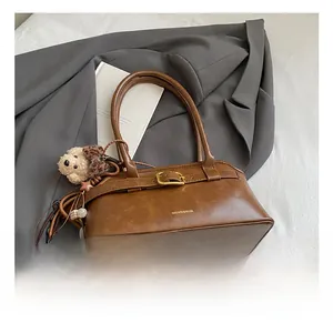 Dettaglio borsa marrone con fibbia dorata e ciondolo orsetto di peluche su tessuto morbido