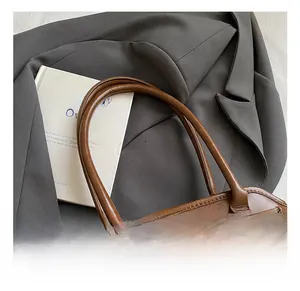 Dettaglio di una borsa tote in pelle marrone vintage con fibbia dorata e doppi manici su blazer
