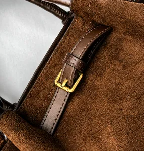 Detail of brown suede bucket bag featuring smooth leather strap and gold buckle