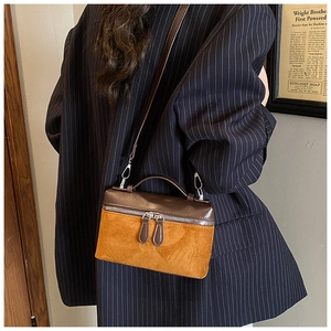 Détail du sac à bandoulière bicolore en cuir marron et daim sur un blazer bleu marine