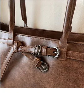 Detail of vintage brown tote bag featuring metal buckle strap and textured leather finish