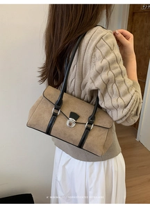 Detail of retro tan suede shoulder bag with black strap worn by a model in a minimal setting