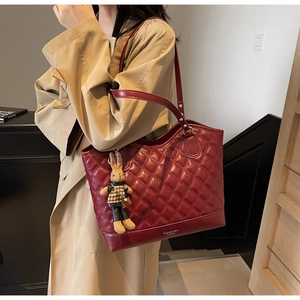 Detail of burgundy quilted tote bag featuring a cute rabbit charm and gold fashion text