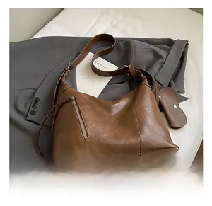 Detail view of brown textured leather crescent bag with decorative silver zipper and heart charm