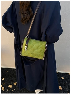 Detail of green quilted nylon barrel bag with brown leather strap and metal rivets