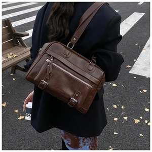 Close-up of a brown PU leather tote bag with silver zippers in a city street setting