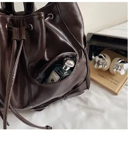 Detail of dark brown leather tote bag showing an external pocket holding a perfume bottle