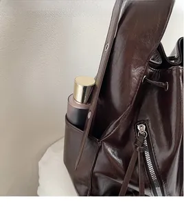 Detail of deep brown glossy oil wax leather bucket bag showing side pocket and texture