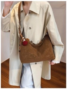 Detail of a large brown suede hobo tote bag featuring a decorative pompom and bead charm