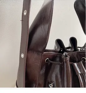 Detail of dark brown glossy bucket bag featuring drawstring closure and metal eyelets