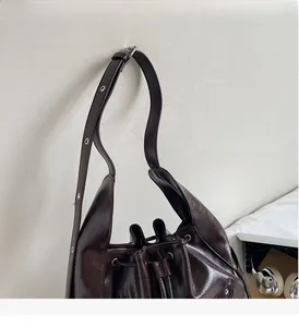 Detail of dark brown bucket bag featuring a drawstring closure and adjustable metal buckle strap