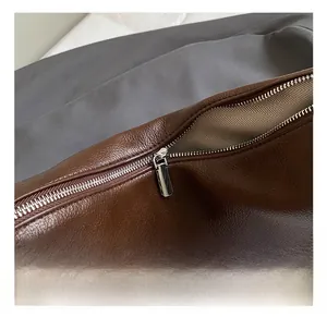 Close-up of brown leather tote bag showing silver metal zipper and V-pattern lining