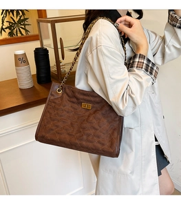 Detail of dark brown quilted suede tote bag with gold chain strap and turn-lock closure