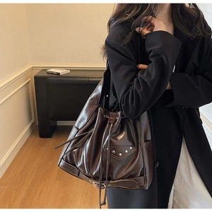 Macro detail of dark brown leather bucket bag featuring metal rivets and decorative zippers