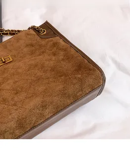 Detail of brown suede tote bag with diamond quilting and gold chain strap and buckle